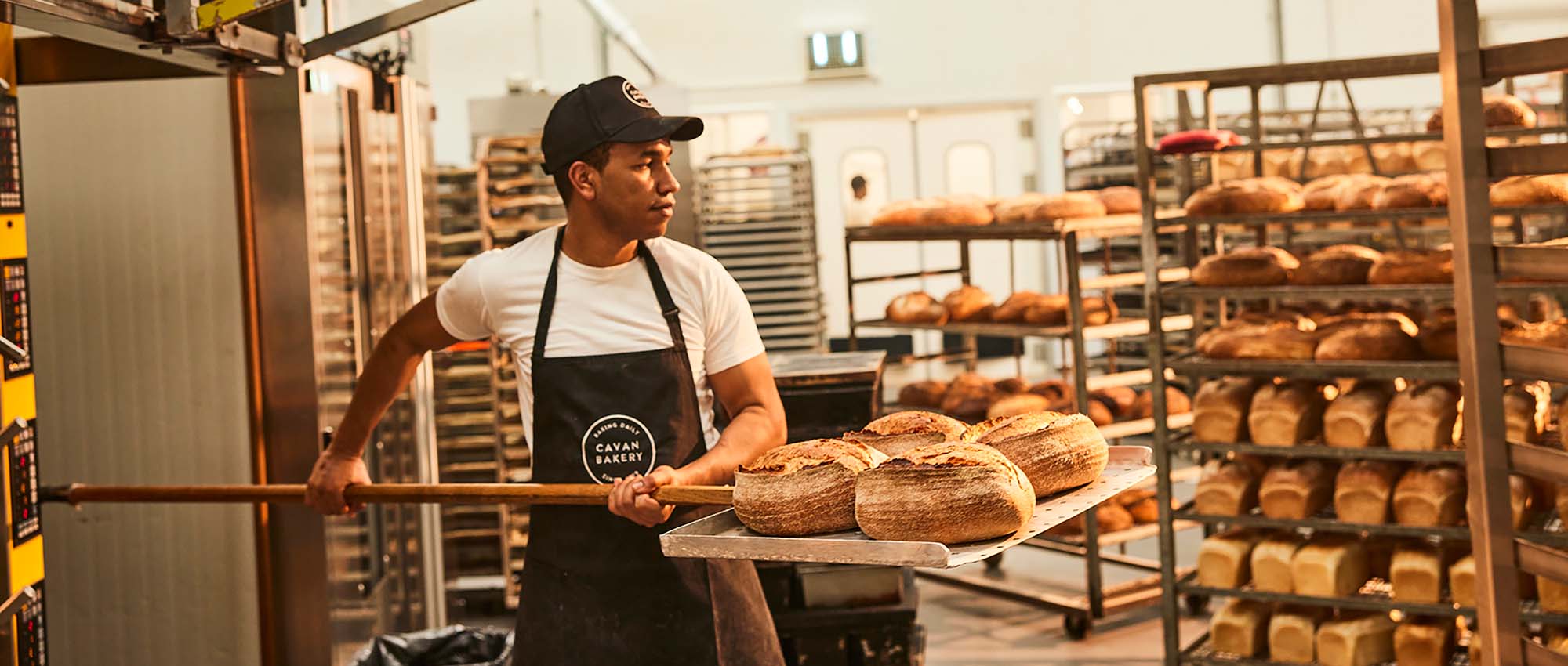 A baker holding a peel with loaves of bread on it.