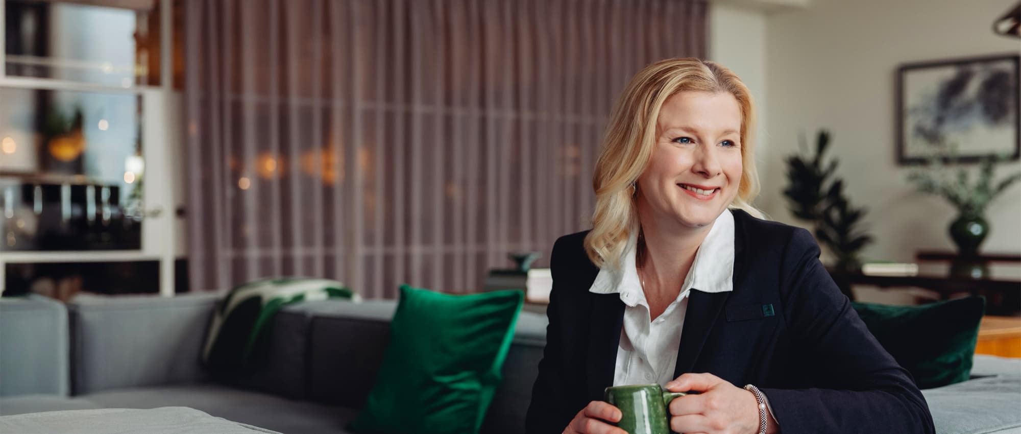 Image of a woman, smiling while drinking coffee